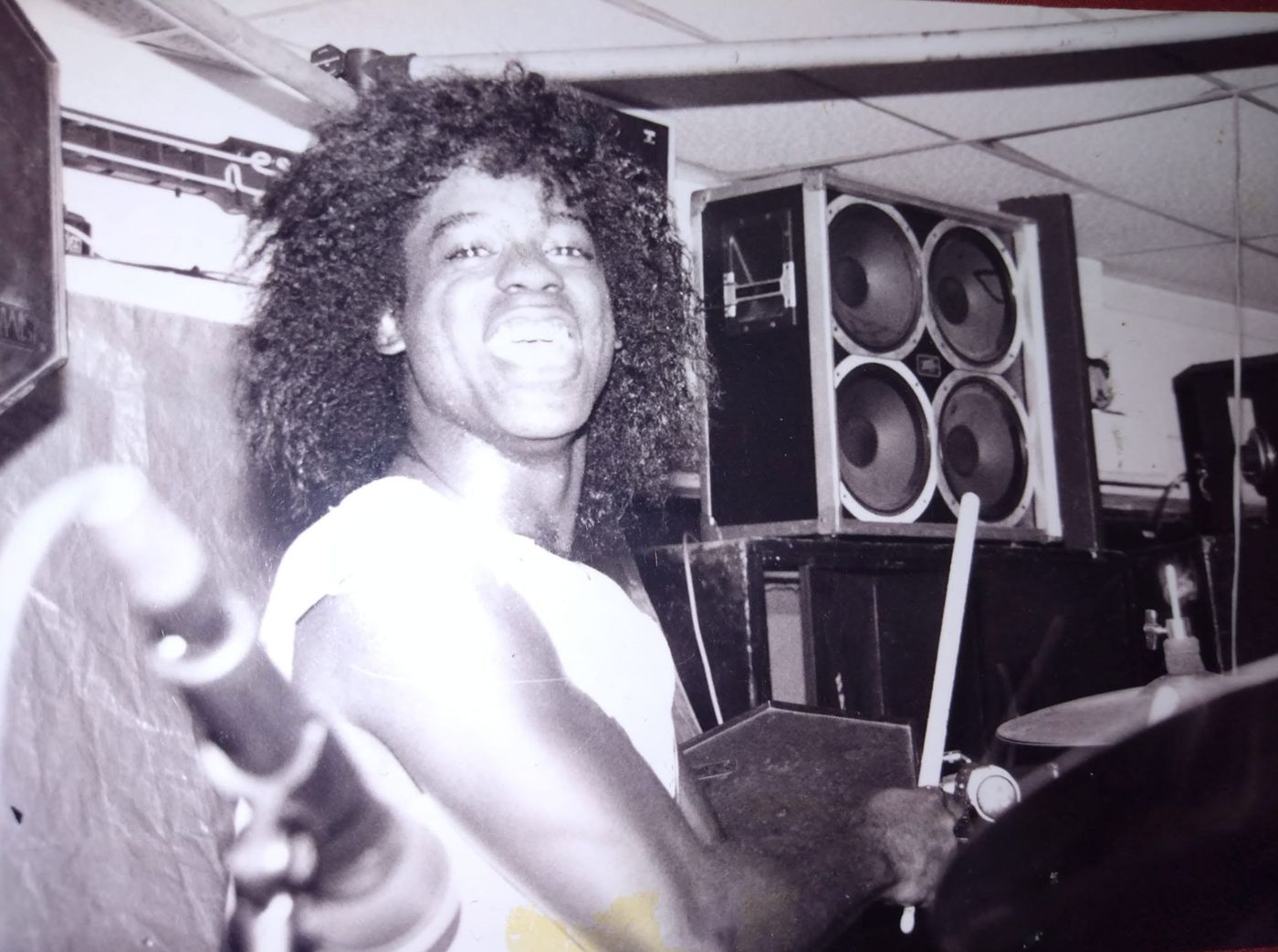 Young Robert with drumsticks in front of speaker stacks, black and white
