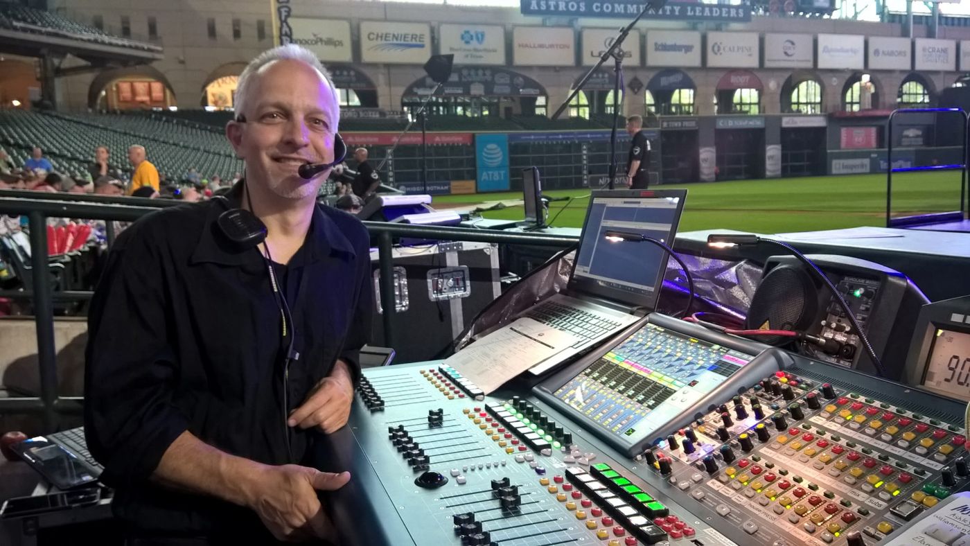 Ed Vertuno smiling at a digital mixing console, wearing a headset