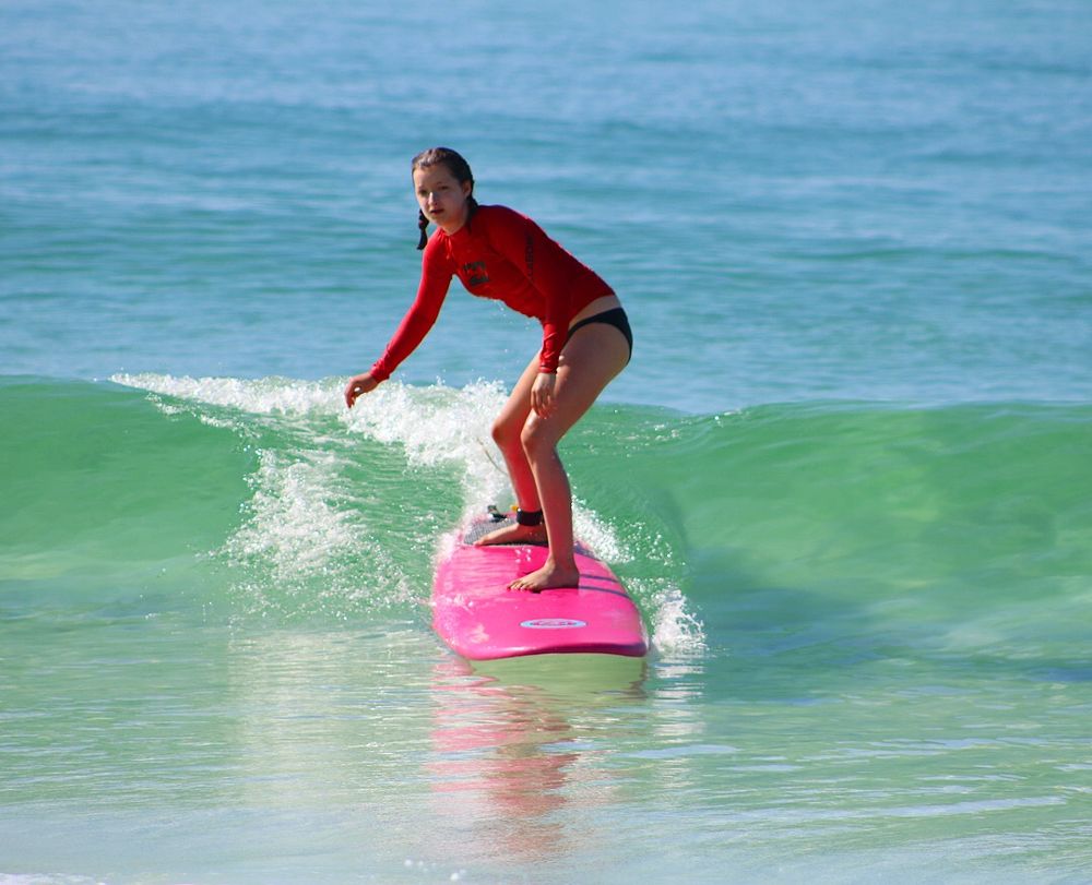 A girl in a red rash guard riding a pink surfboard